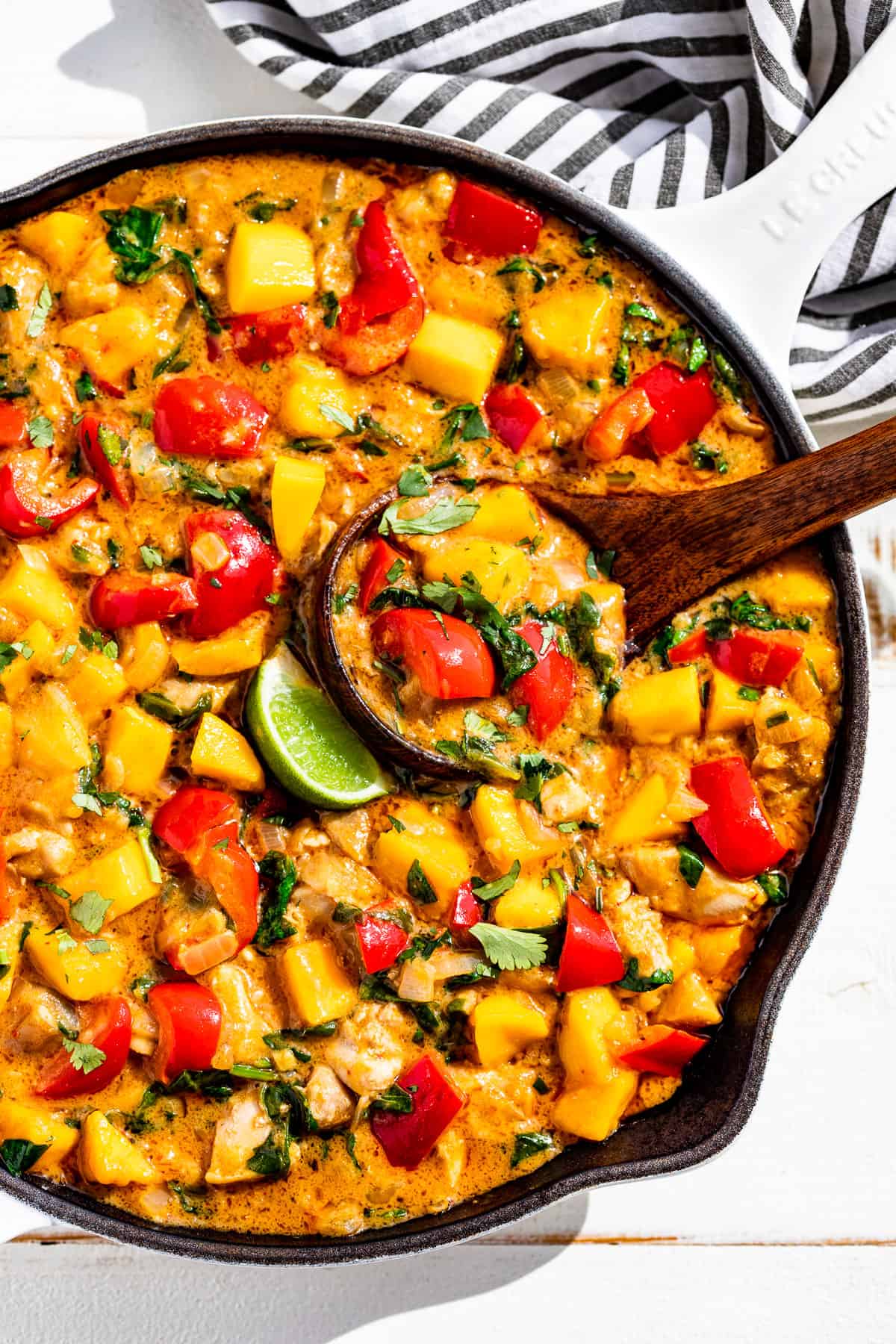 Mango Chicken Curry in a with skillet with a wood ladle scooping some out.