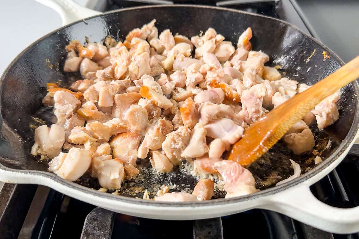 Sautéing the cubed chicken thighs in a white enameled cast iron skillet.