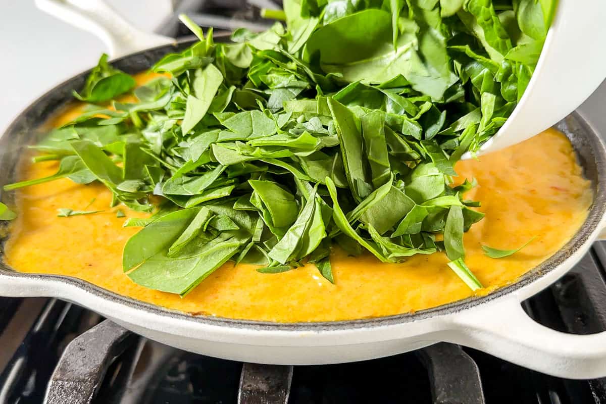 Adding the chopped spinach to the curry near the end of the cooking time.