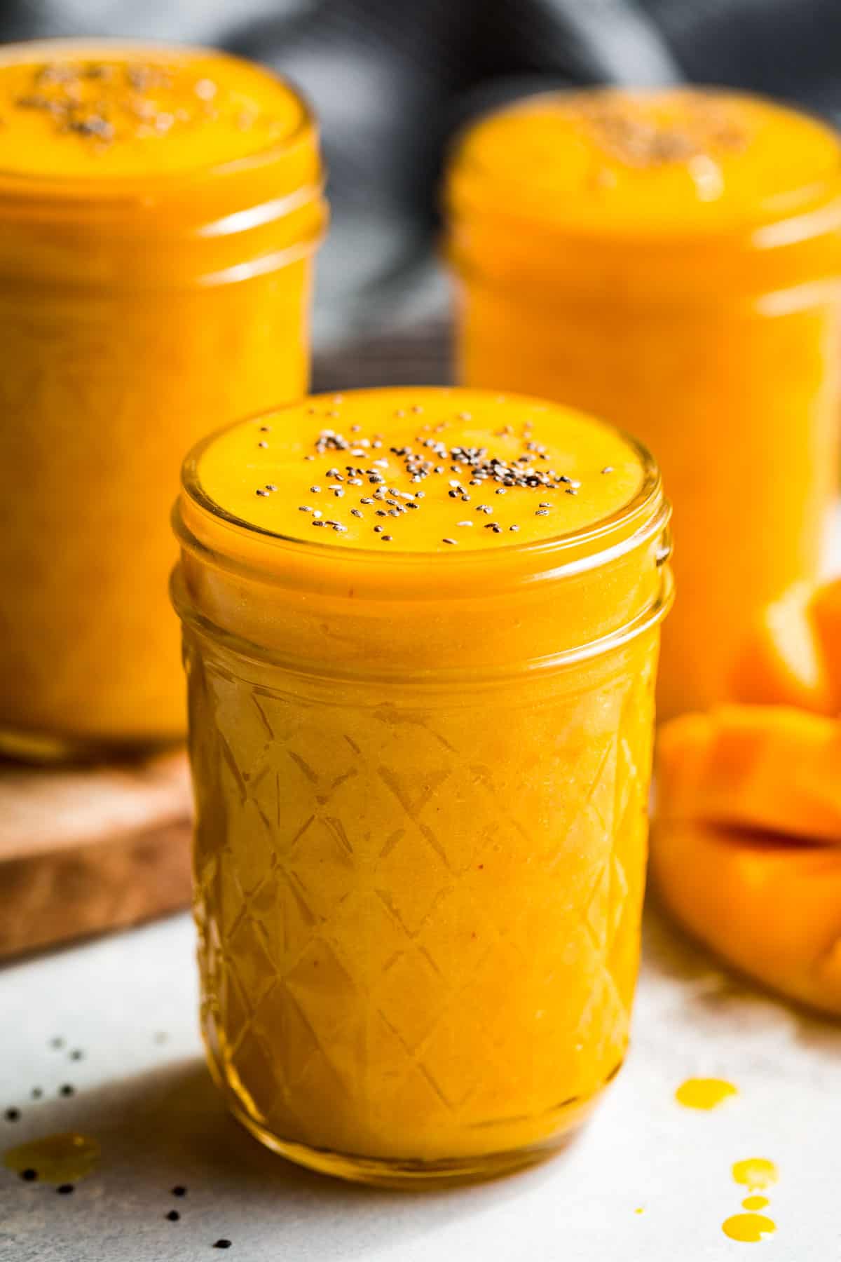 Three glasses of Mango Smoothie with a diced mango on the side and a blue linen in the background.