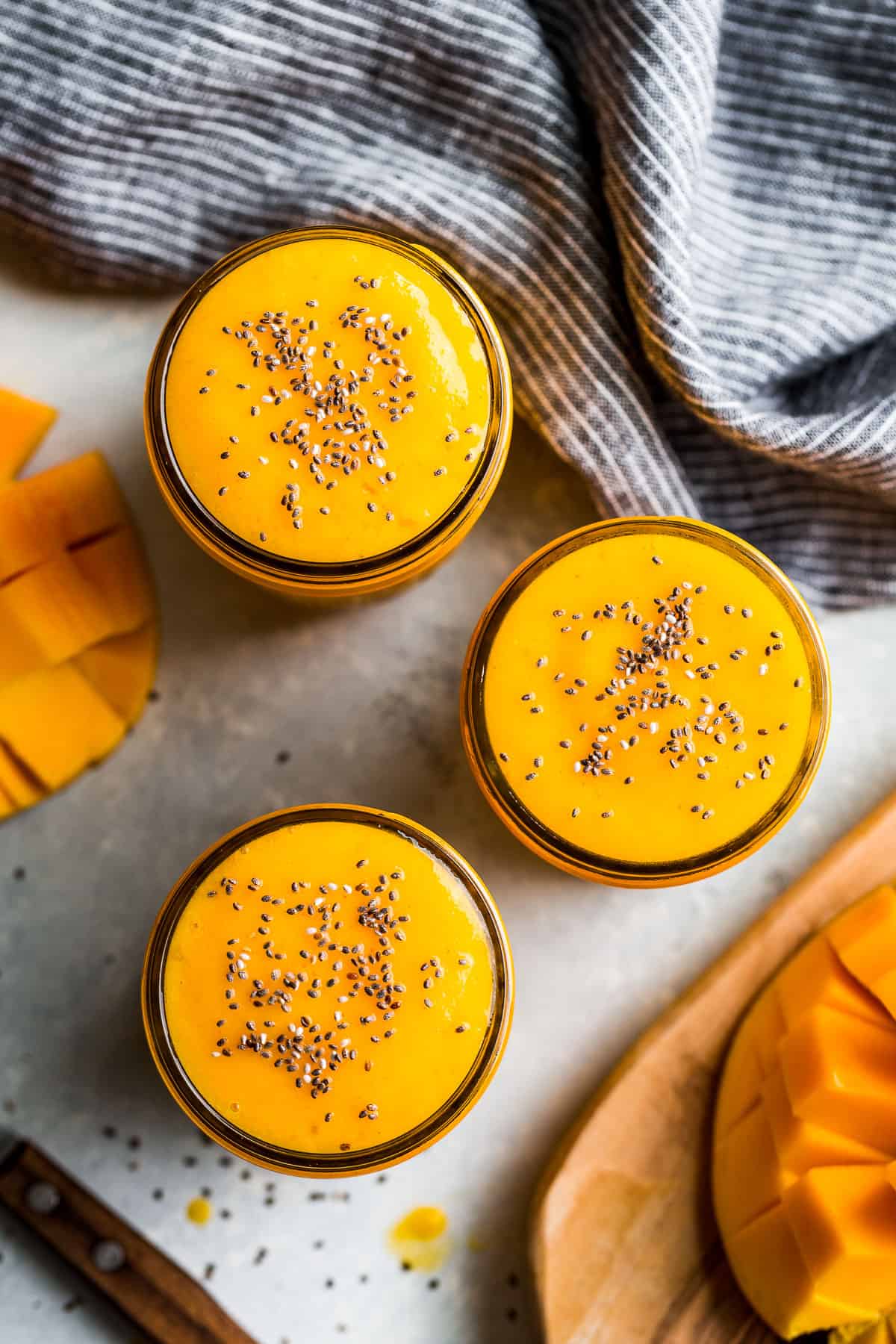 Straight down view of three glasses of mango smoothie with a blue linen in the background.