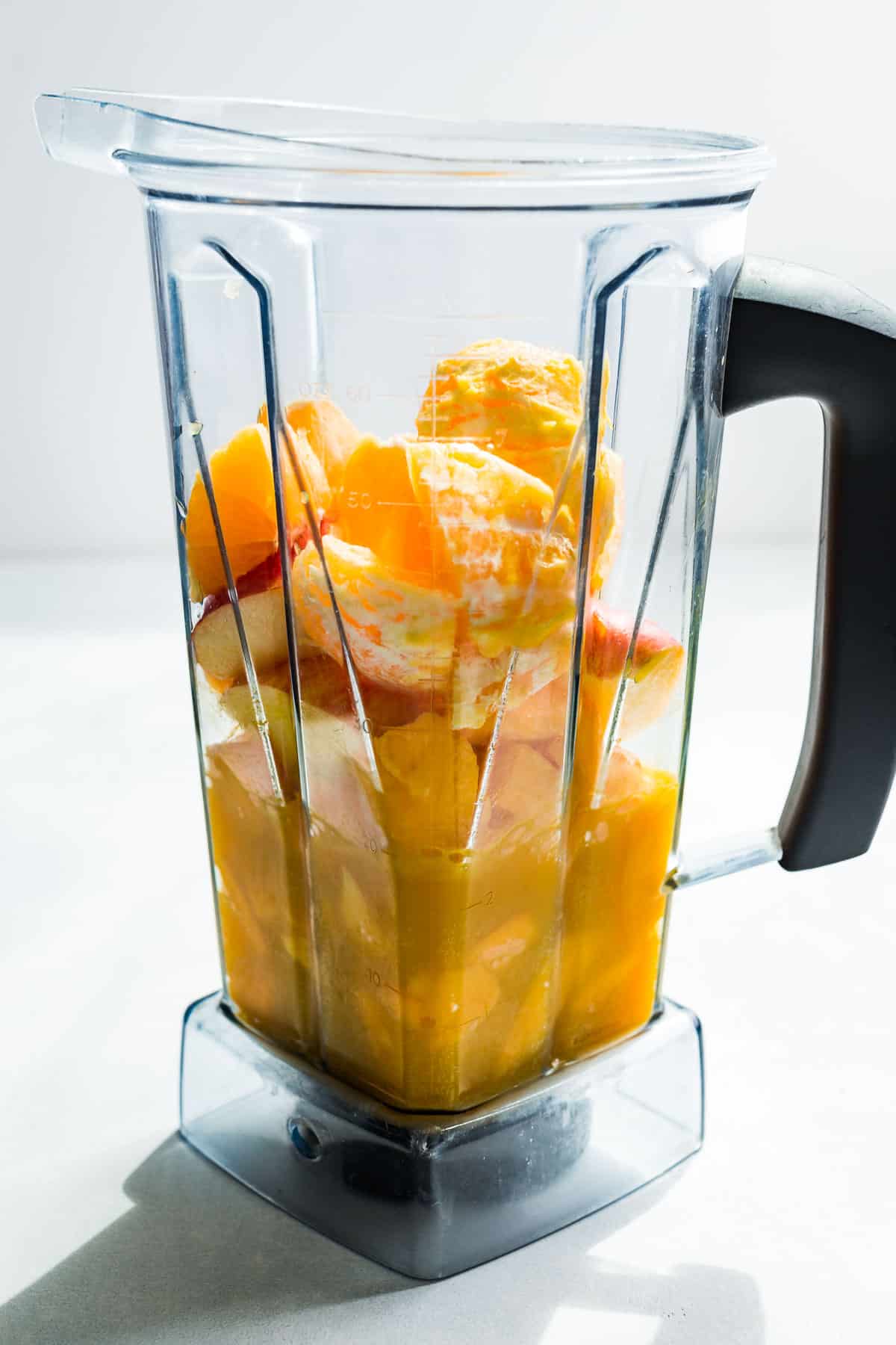 The mango, orange, apple, and orange juice added to a blender container.
