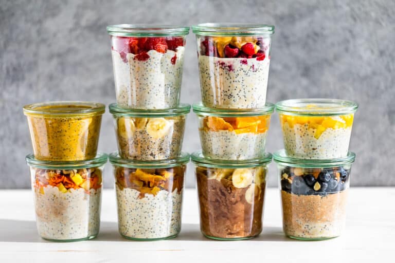 All 10 flavors of overnight oats in clear glass jar on a white board with a grey background