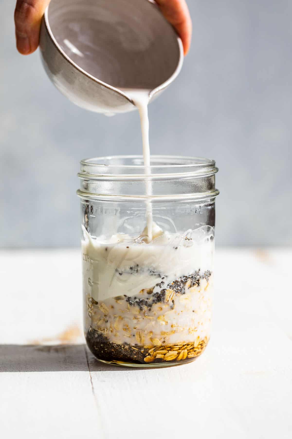 Adding the milk to the overnight oats ingredients in a mason jar.