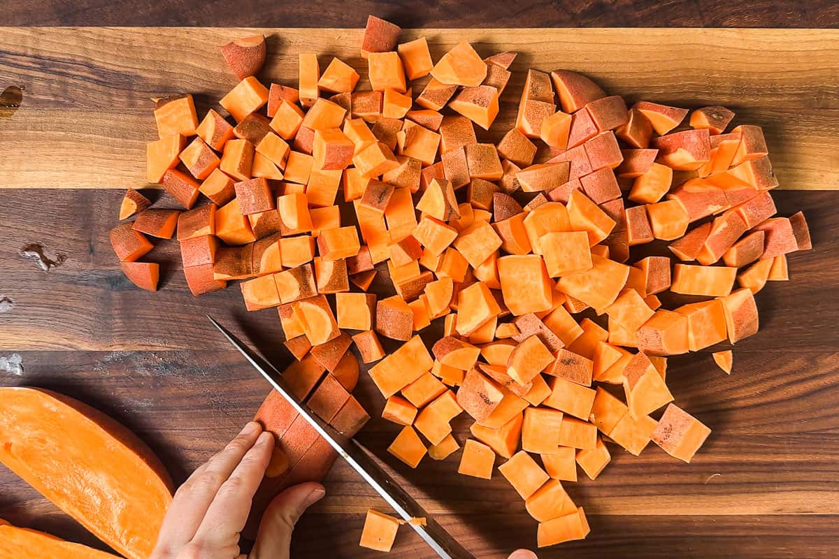 Cubing up sweet potatoes on a wood cutting board.