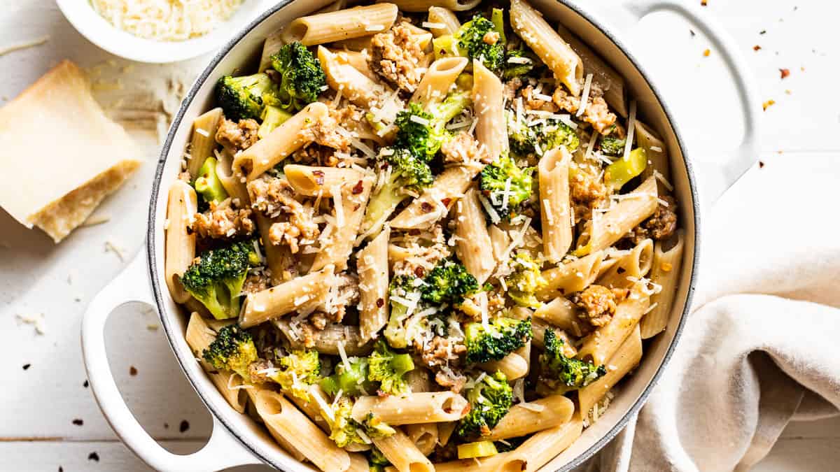 Sausage Broccoli Pasta in a large white pot with grated parmesan cheese on the side.