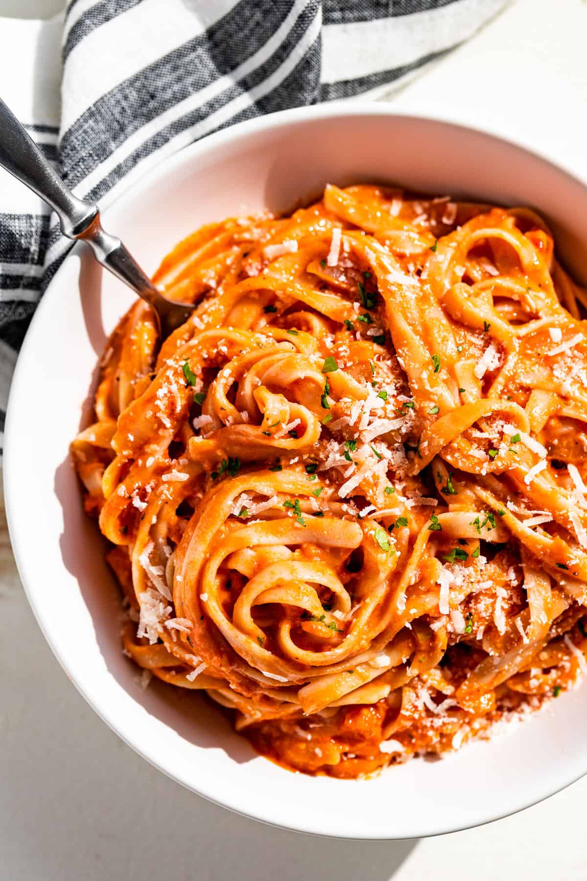 Straight down view of tomato cream sauce tossed together with fettuccini and sprinkled with parmesan cheese.