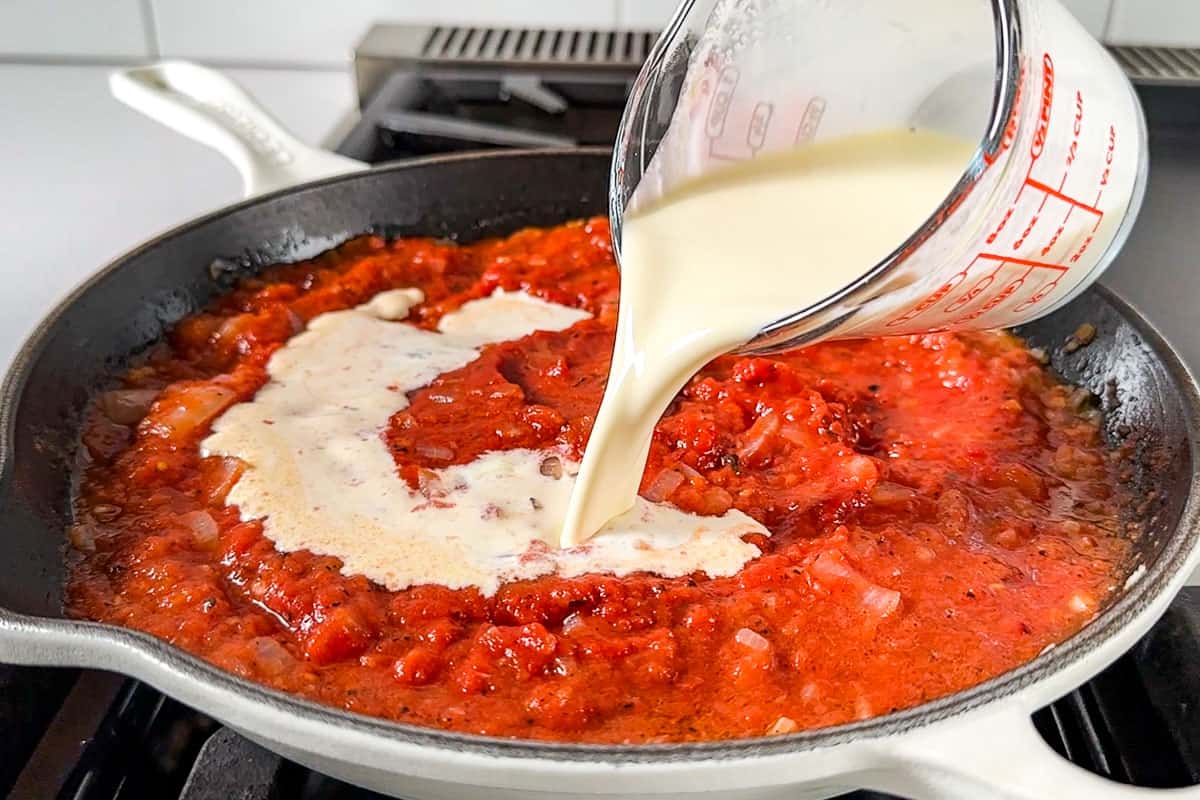 Adding the cream to the tomato sauce in a white cast iron skillet.