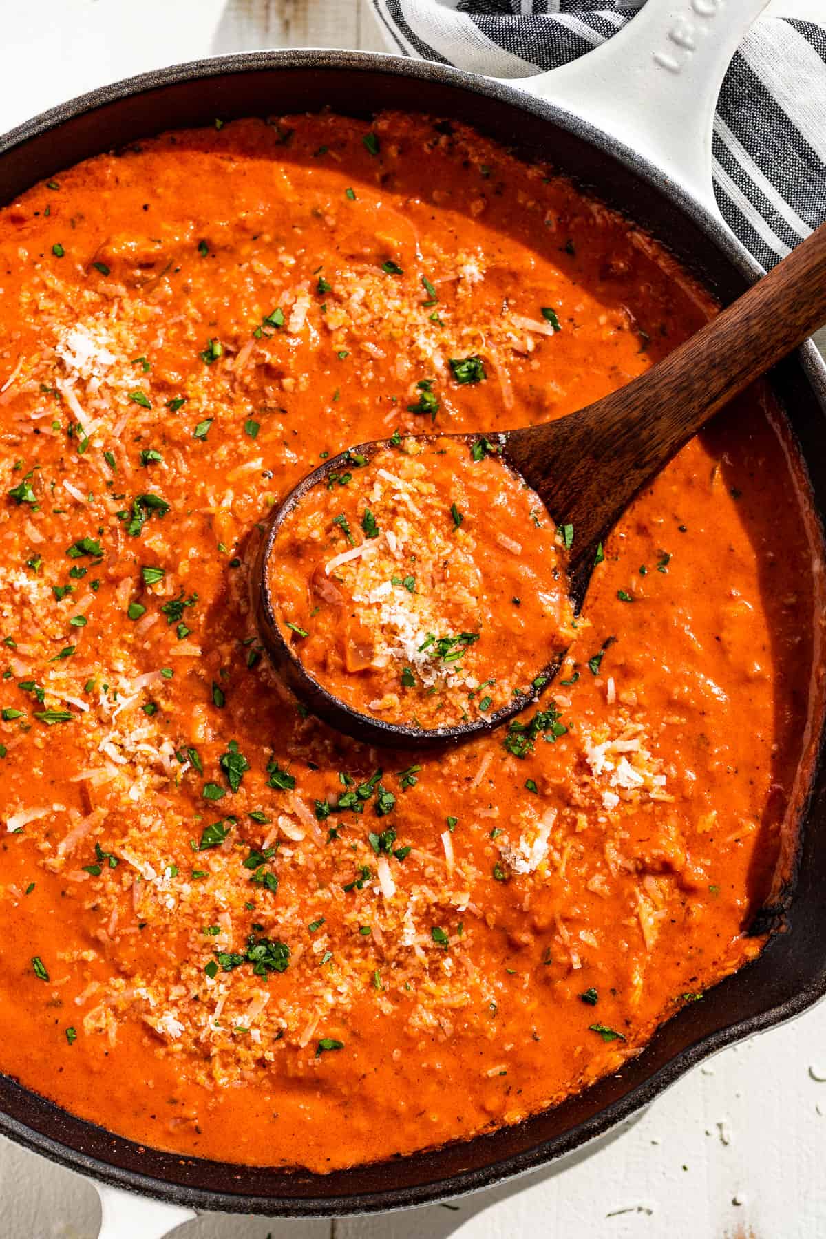 Straight down view of Tomato Cream Sauce in a white cast iron skillet sprinkles with parmesan cheese and parsley.