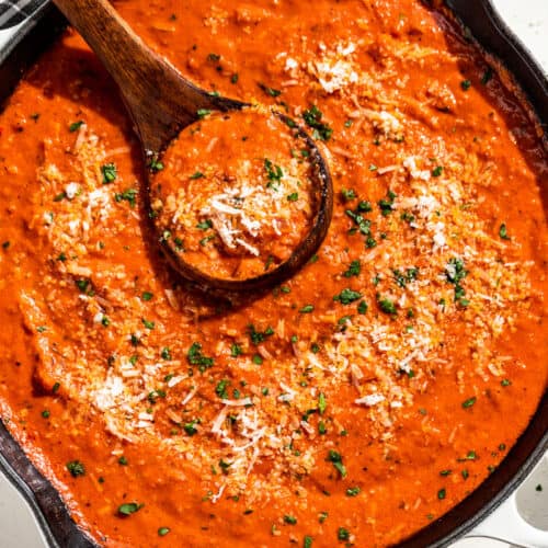 Downwards view of finished Tomato Cream Sauce in a skillet with a wood ladle and sprinkled with parmesan and parsley.