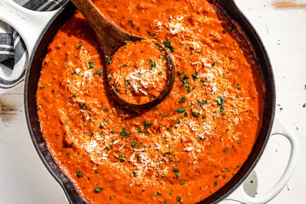 Downwards view of finished Tomato Cream Sauce in a skillet with a wood ladle and sprinkled with parmesan and parsley.