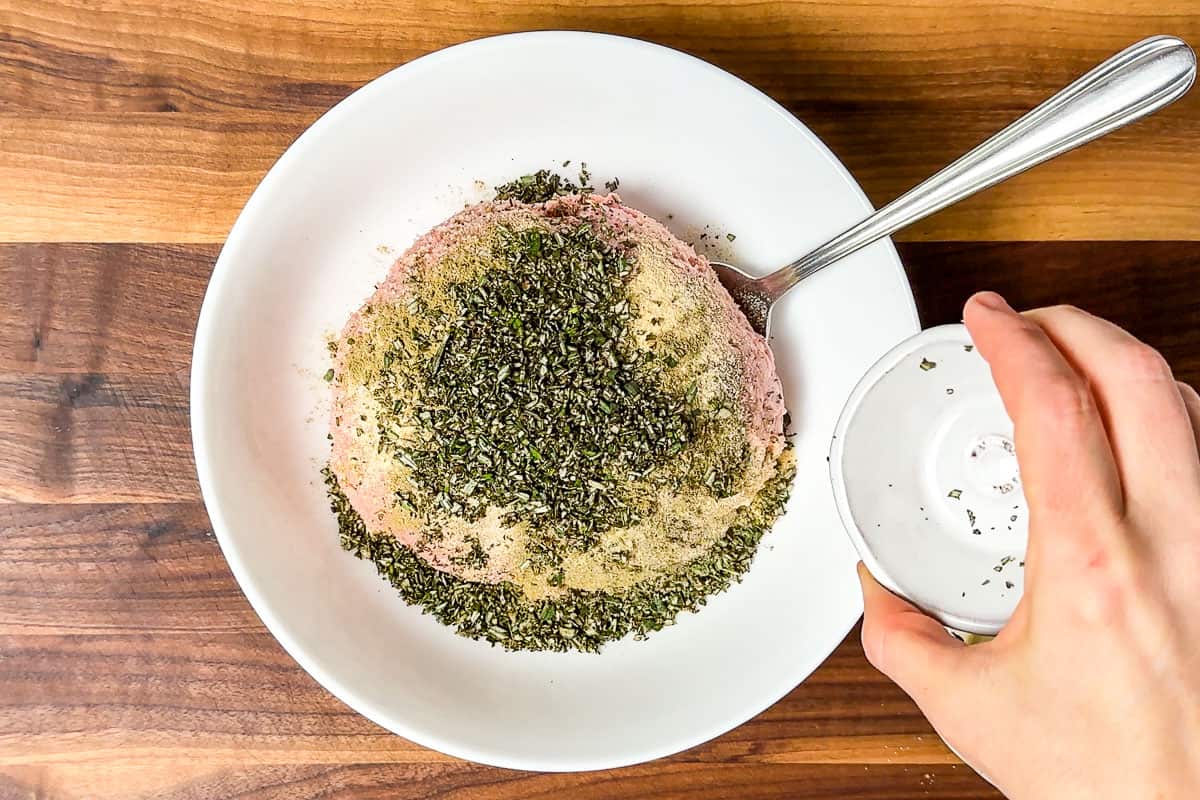 Adding the herbs to a white bowl with the ground turkey.
