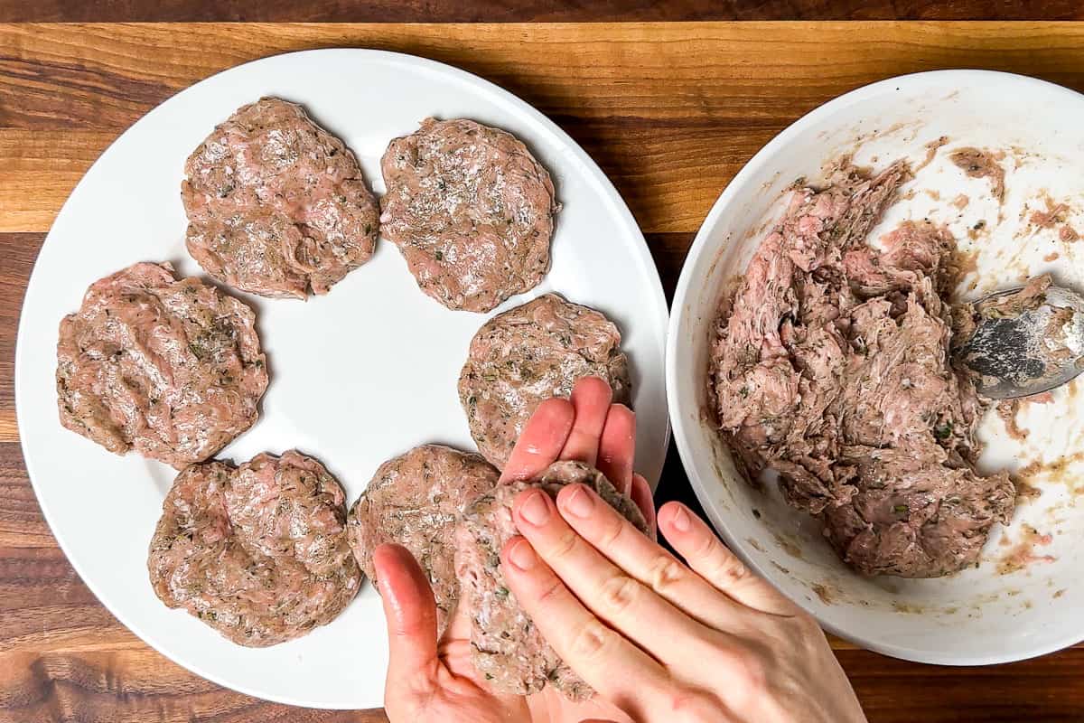 Forming the Turkey Breakfast Sausage into patties on a white plate sitting on a wood cutting board.