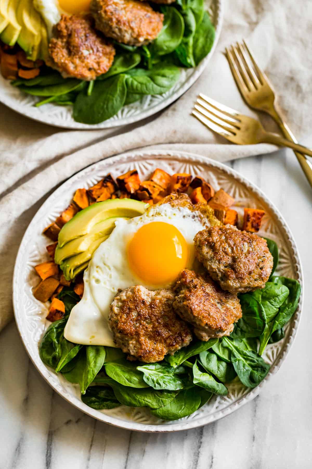 Turkey Breakfast Sausage patties on a bed of spinach with roasted sweet potatoes and an over easy egg on top with sliced avocado.