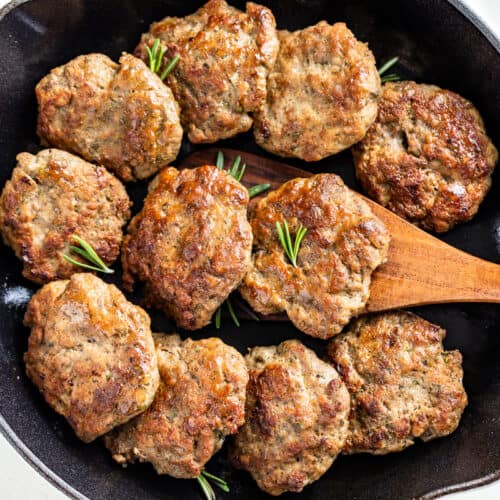 Straight down view of browned Turkey Sausage patties in a white enameled cast iron skillet with a wood spatula scooping one out.