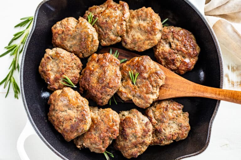 Straight down view of browned Turkey Sausage patties in a white enameled cast iron skillet with a wood spatula scooping one out.