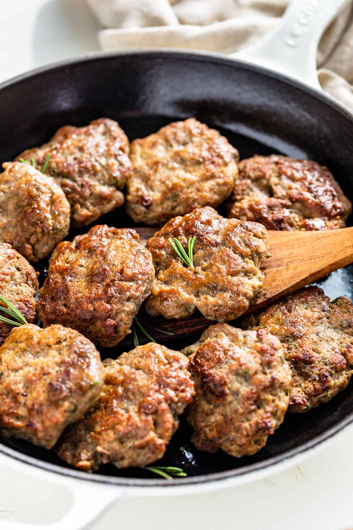 Side view of Turkey Breakfast Sausage cooked into browned patties in a skillet with a wood spatula.