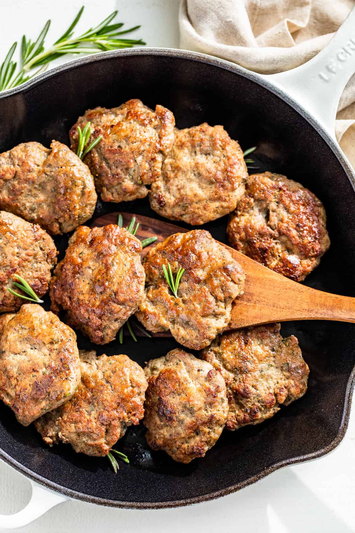 A large enameled white cast iron skillet with Turkey Breakfast Sausage in it with a wood spatula scooping one out.