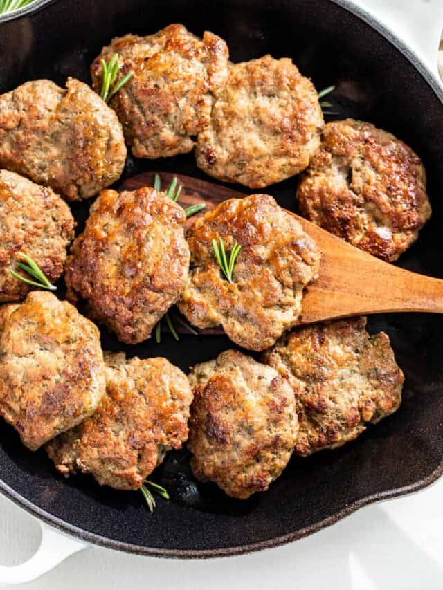 A large enameled white cast iron skillet with Turkey Breakfast Sausage in it with a wood spatula scooping one out.