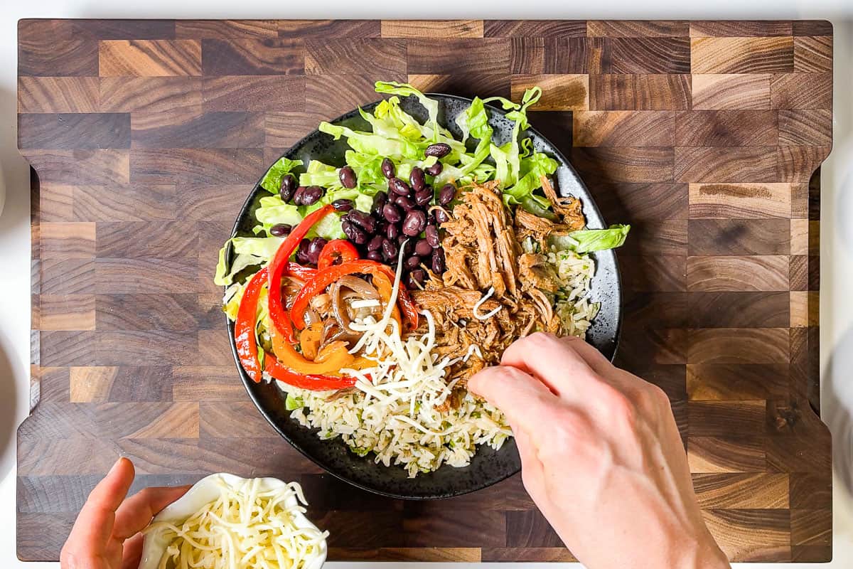 Sprinkling cheese over the Carnitas Burrito Bowls on a wood cutting board.