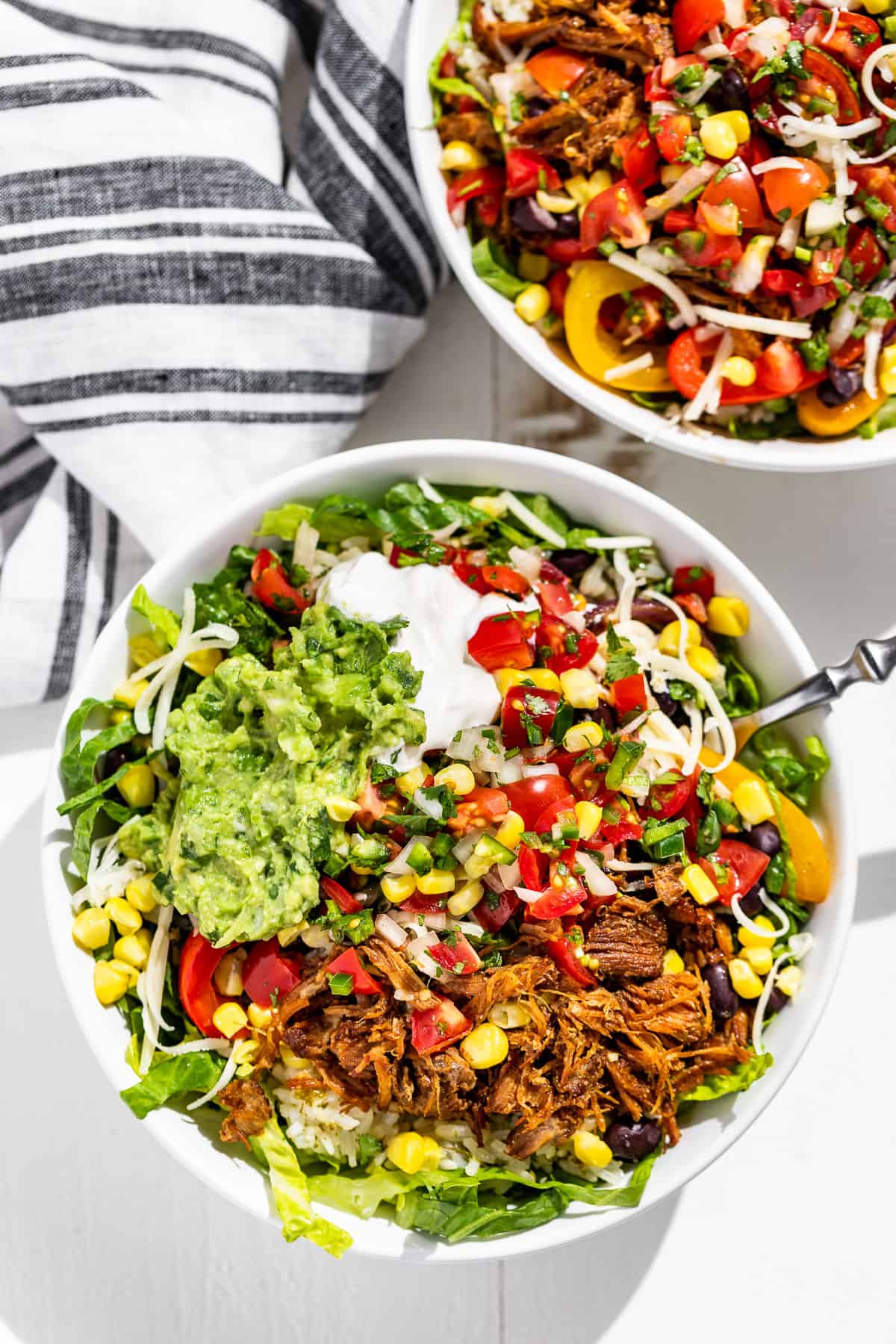 Straight down view of 2 Carnitas Burrito Bowls with a blue and white striped linen on the side.