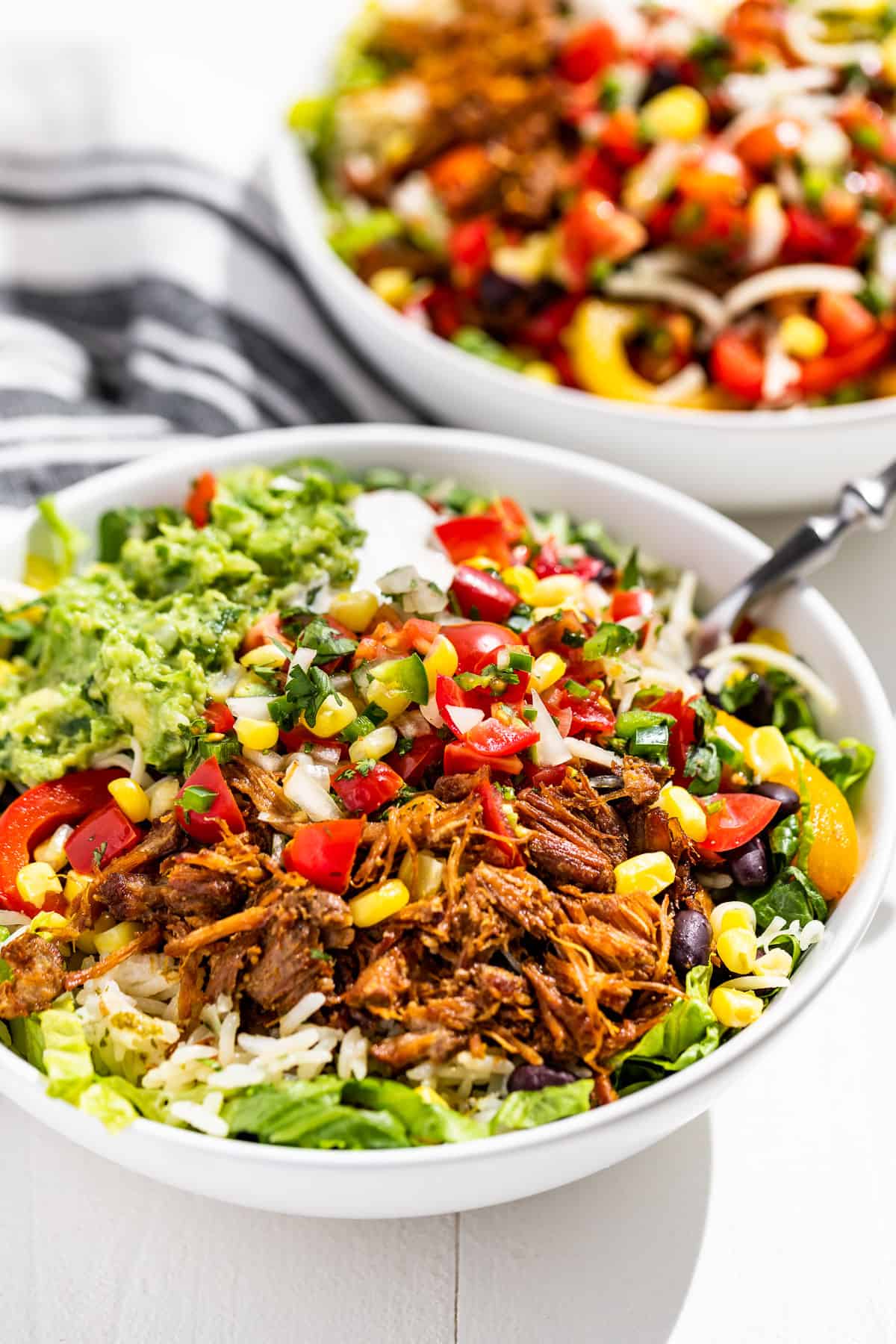 Close up side view of Carnitas Burrito Bowls with a blue and white striped linen in the background.