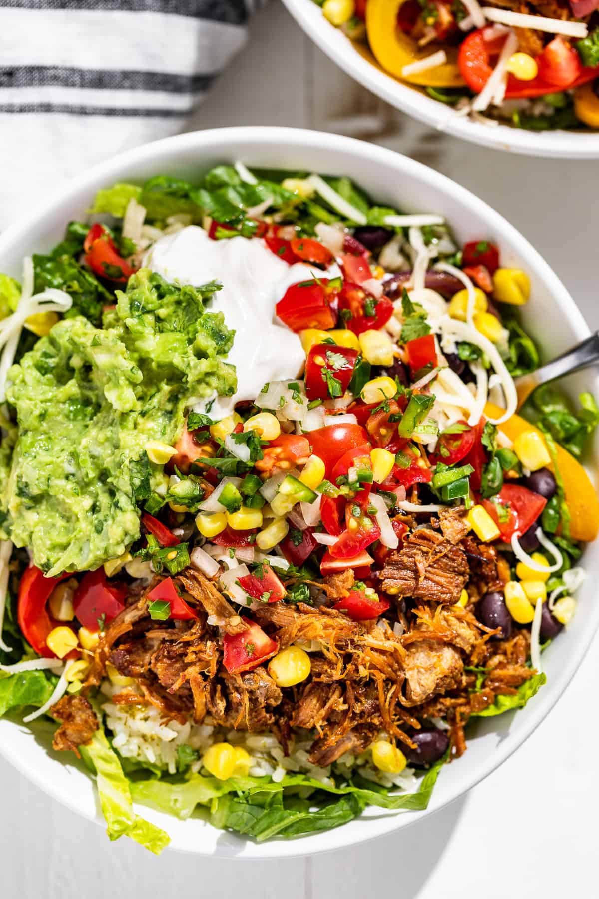 Close up straight down view of two Carnitas Burrito Bowls with a fork in one.