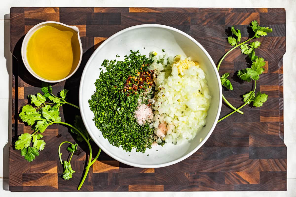 Adding the chopped cilantro, onion, and garlic to a white bowl set on a wood cutting board.