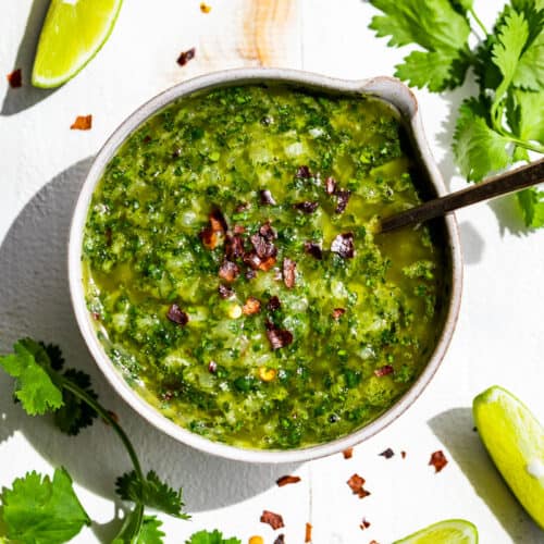 Straight down view of Cilantro Chimichurri in a small pottery bowl with a silver spoon in it and cilantro sprigs on the side.