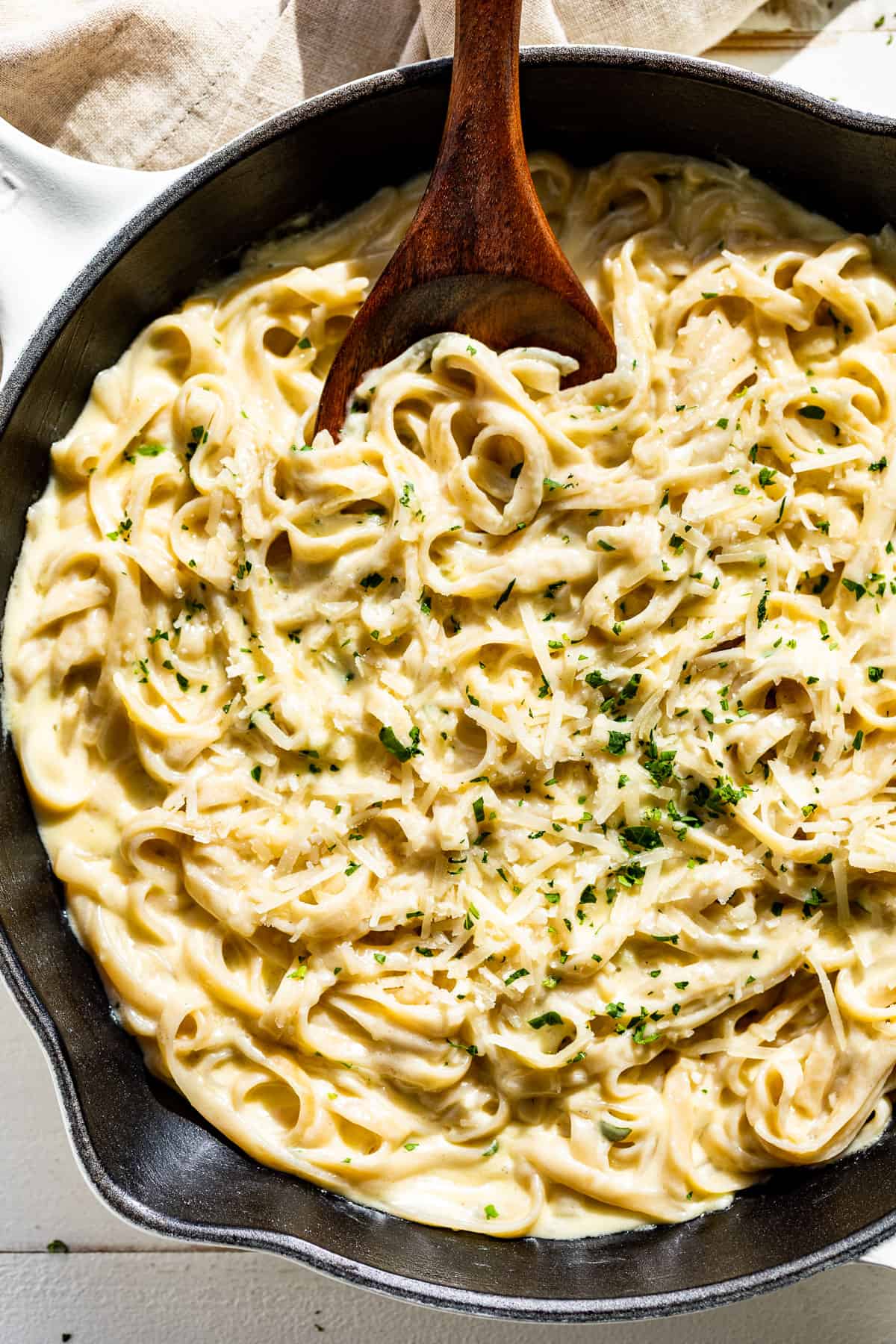 Straight down view of Garlic Parmesan Pasta in a white skillet with a wood spoon scooping some out.