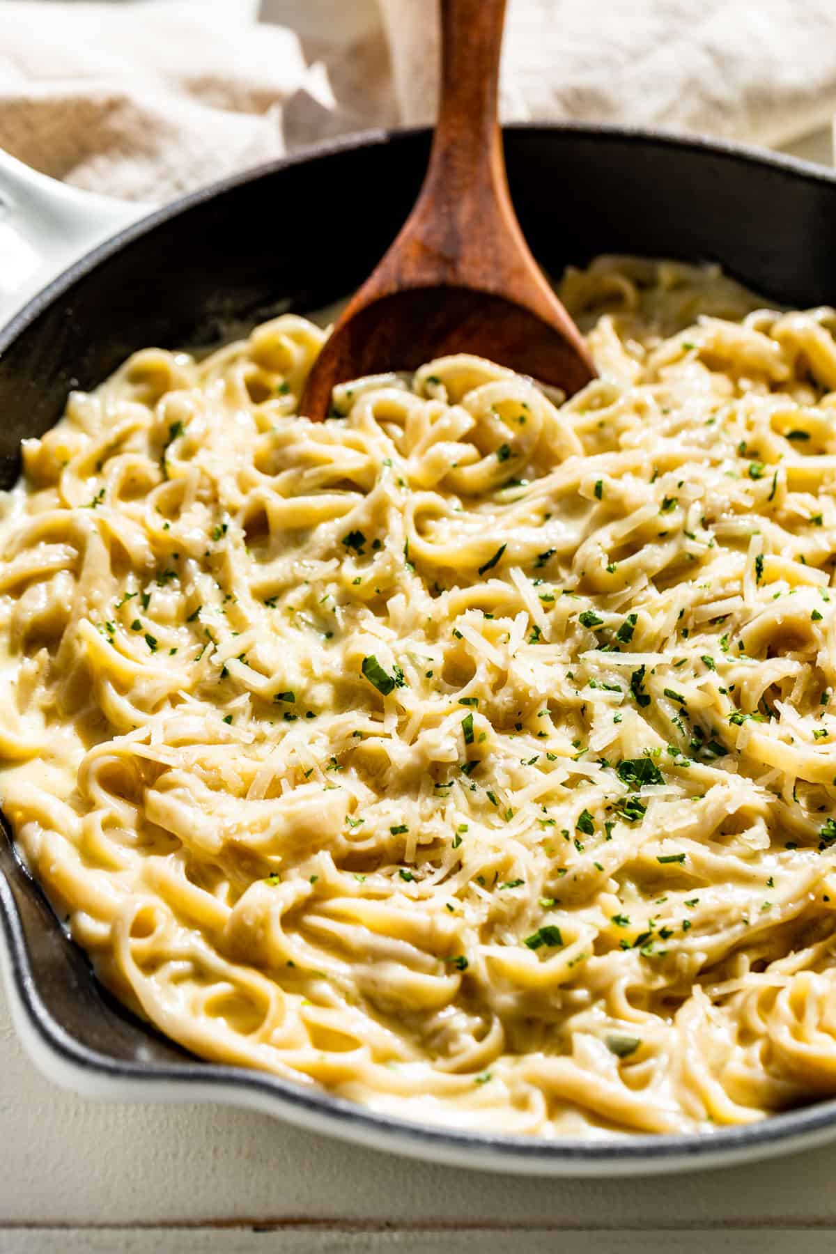 Side view of Garlic Parmesan Pasta in a white skillet with a wood spoon scooping some out.