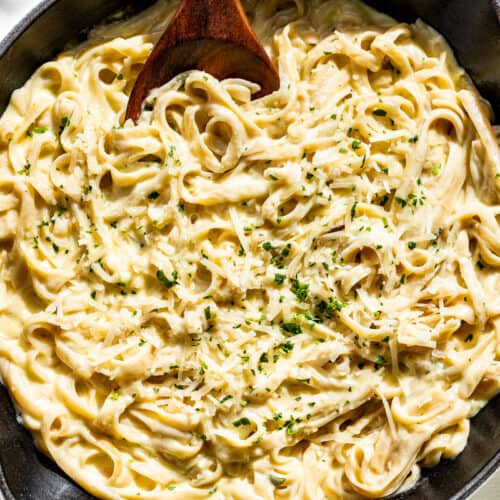 The linguine pasta tossed together with the garlic cream sauce in a large white skillet sprinkled with chopped parsley.