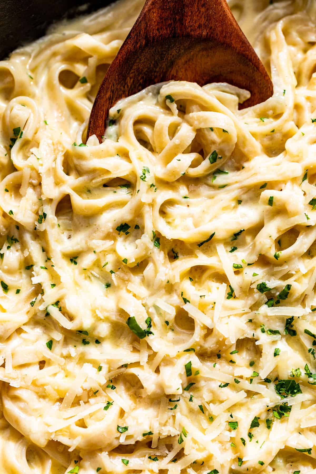 Close macro view of the linguine tossed together with the garlic parmesan sauce with a wood spoon in it.