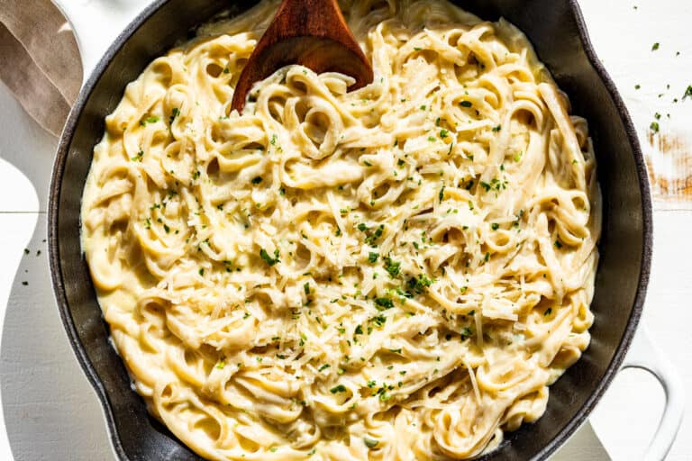 The linguine pasta tossed together with the garlic cream sauce in a large white skillet sprinkled with chopped parsley.