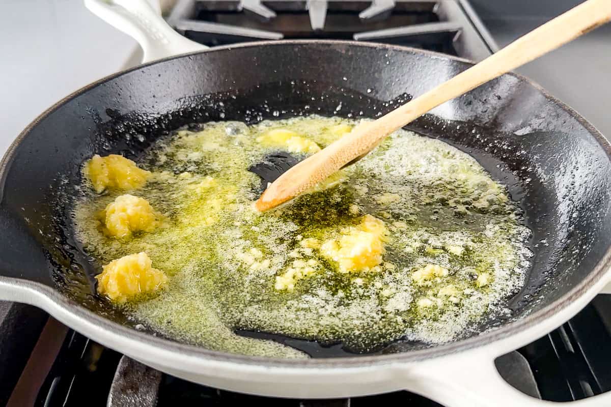 Sautéing garlic in butter in a large white skillet with a wood spoon.