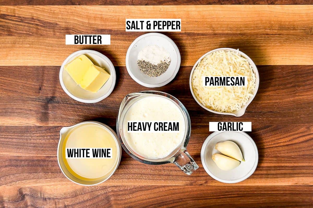 Butter, white wine, heavy whipping cream, garlic, grated parmesan cheese, sea salt, and pepper in small bowls on a wood cutting board.