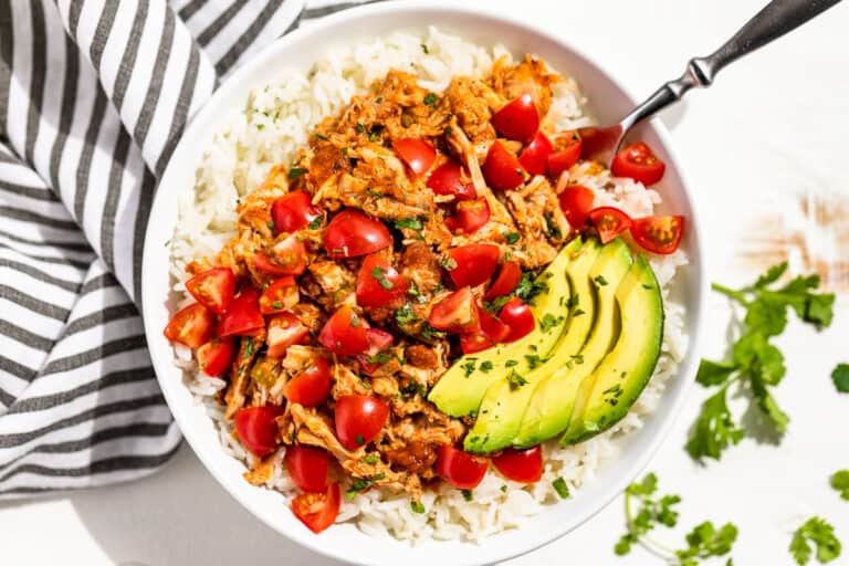 Straight down view of shredded Instant Pot Chicken Tinga piled over steamed rice topped with chopped tomatoes, cilantro, and sliced avocado.