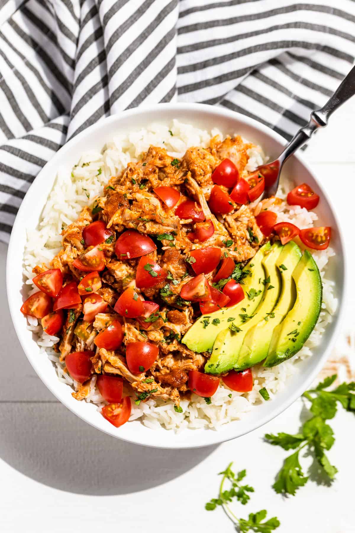 Straight down view of shredded Instant Pot Chicken Tinga piled over steamed rice topped with chopped tomatoes, cilantro, and sliced avocado.