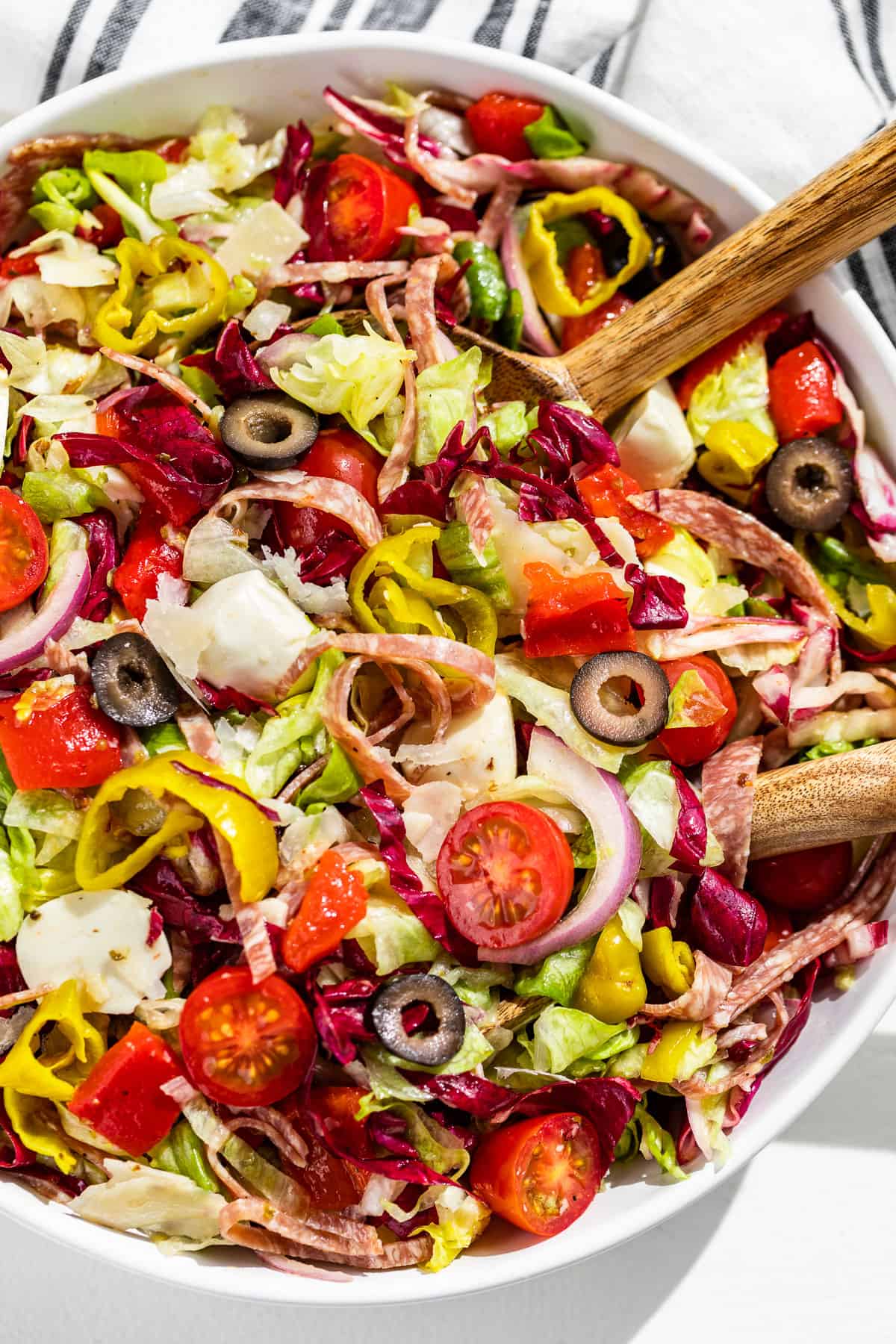 Straight down view of half a large white bowl filled with Italian Chopped Salad and white handled wood serving spoons scooping some out.