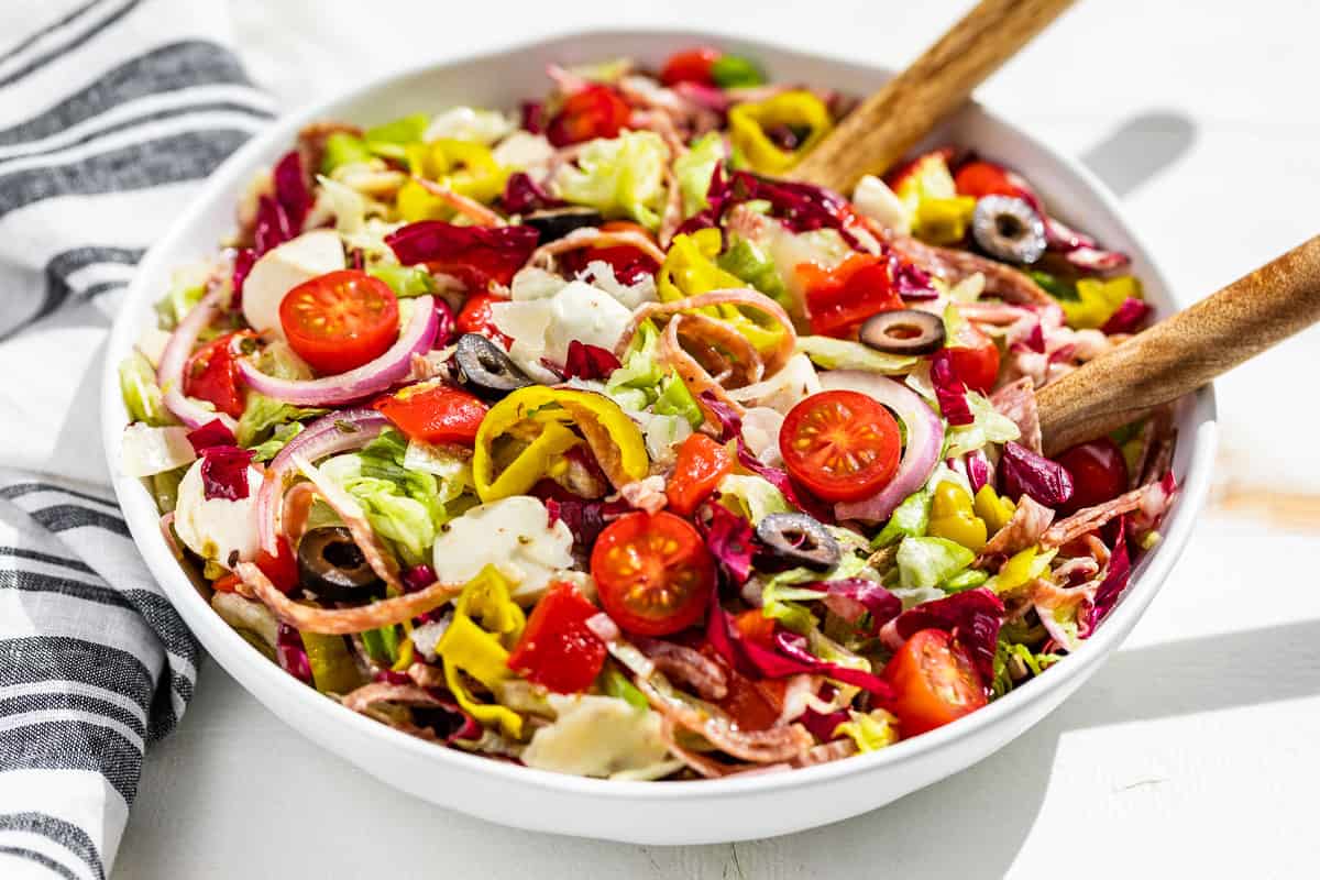 The finished Italian Chopped Salad in a large white serving bowl with white handled wood serving spoons in the side of the dish.