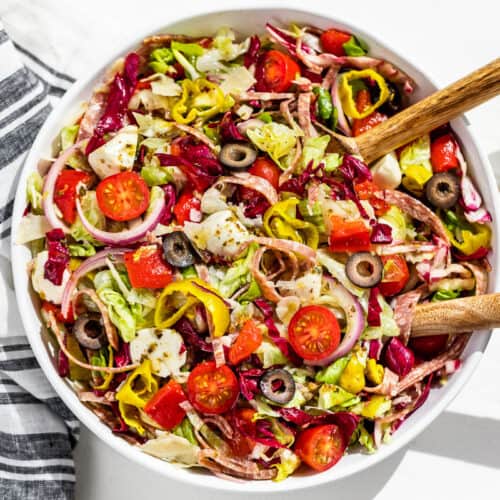 The finished Italian Chopped Salad in a large white serving bowl with white handled wood serving spoons in the side of the dish.