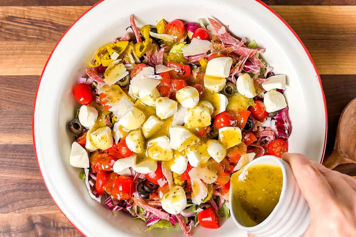 Pouring the dressing over the ingredients for the Italian Chopped Salad in a large serving bowl.