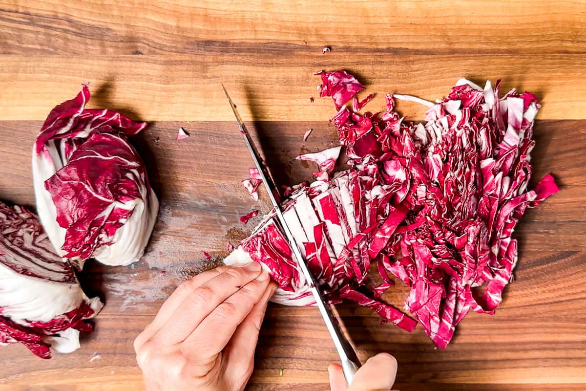 Thinly slicing up the radicchio on a wood cutting board.
