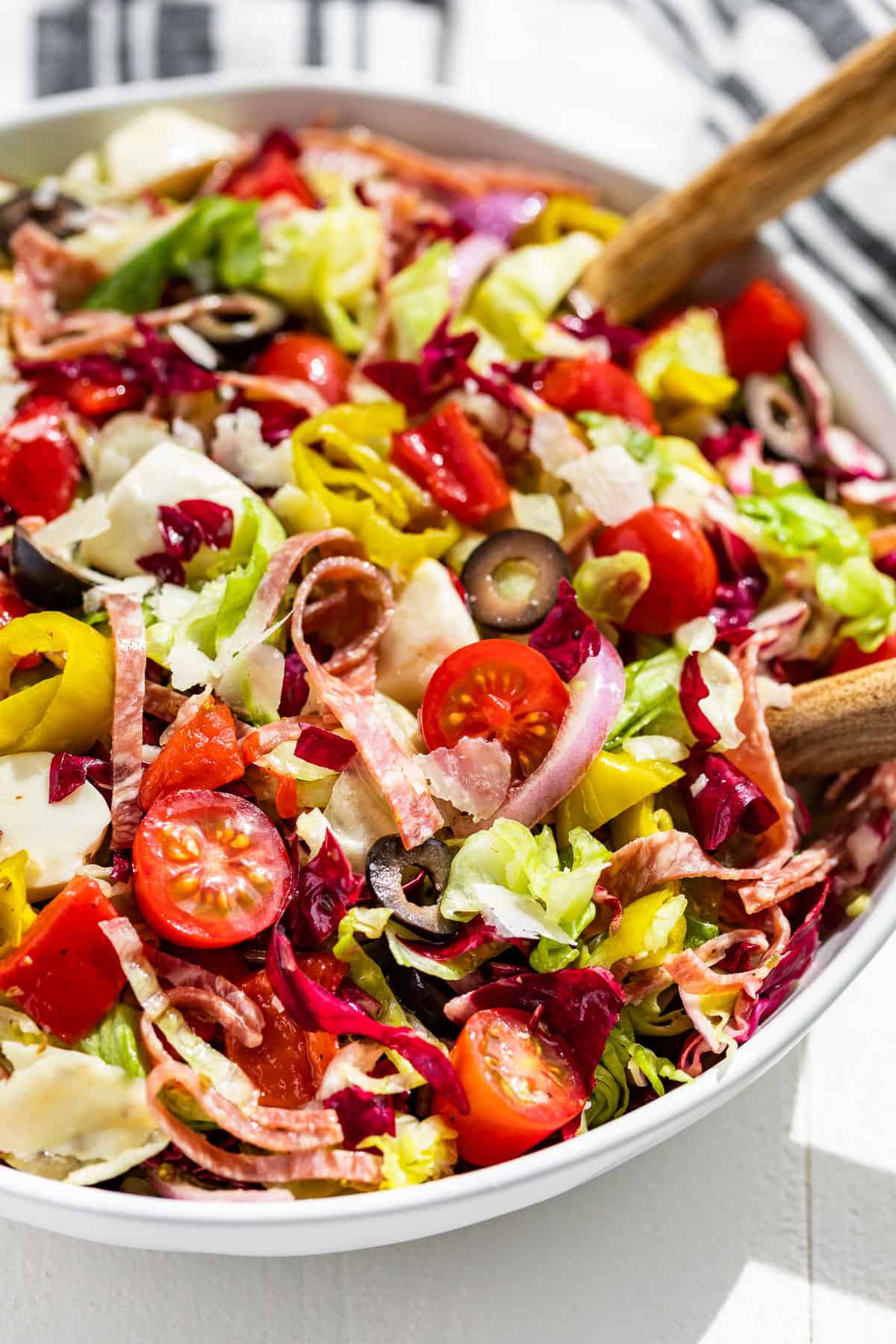 Close side view of Italian Chopped Salad in a white serving bowl with white handled wood serving spoons in the side of the bowl.