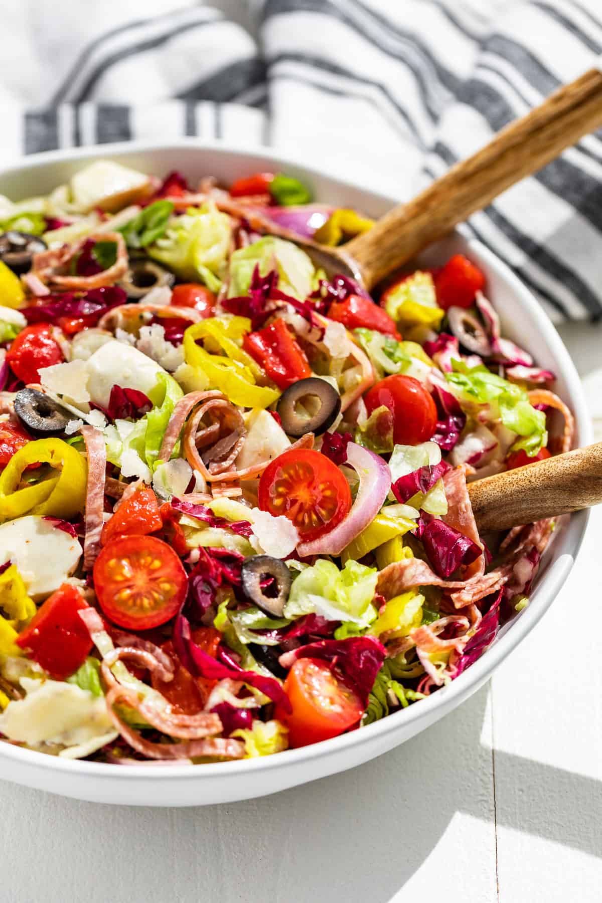 Side view of half a large bowl filled with Italian Chopped Salad with white handled wood serving spoons in the side of the bowl.