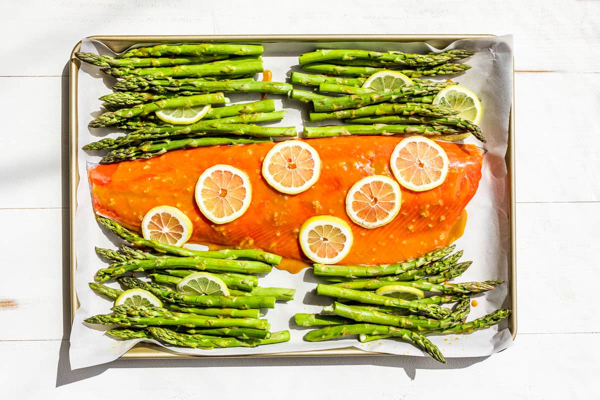 Spreading the honey mustard glaze over the salmon topped with lemon slices and asparagus on the side.
