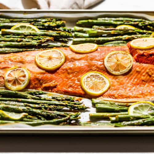 The finished roasted salmon and asparagus with a wood spatula scooping up a piece of salmon.