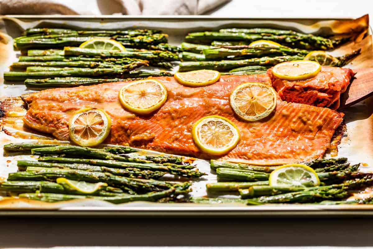 The finished roasted salmon and asparagus with a wood spatula scooping up a piece of salmon.