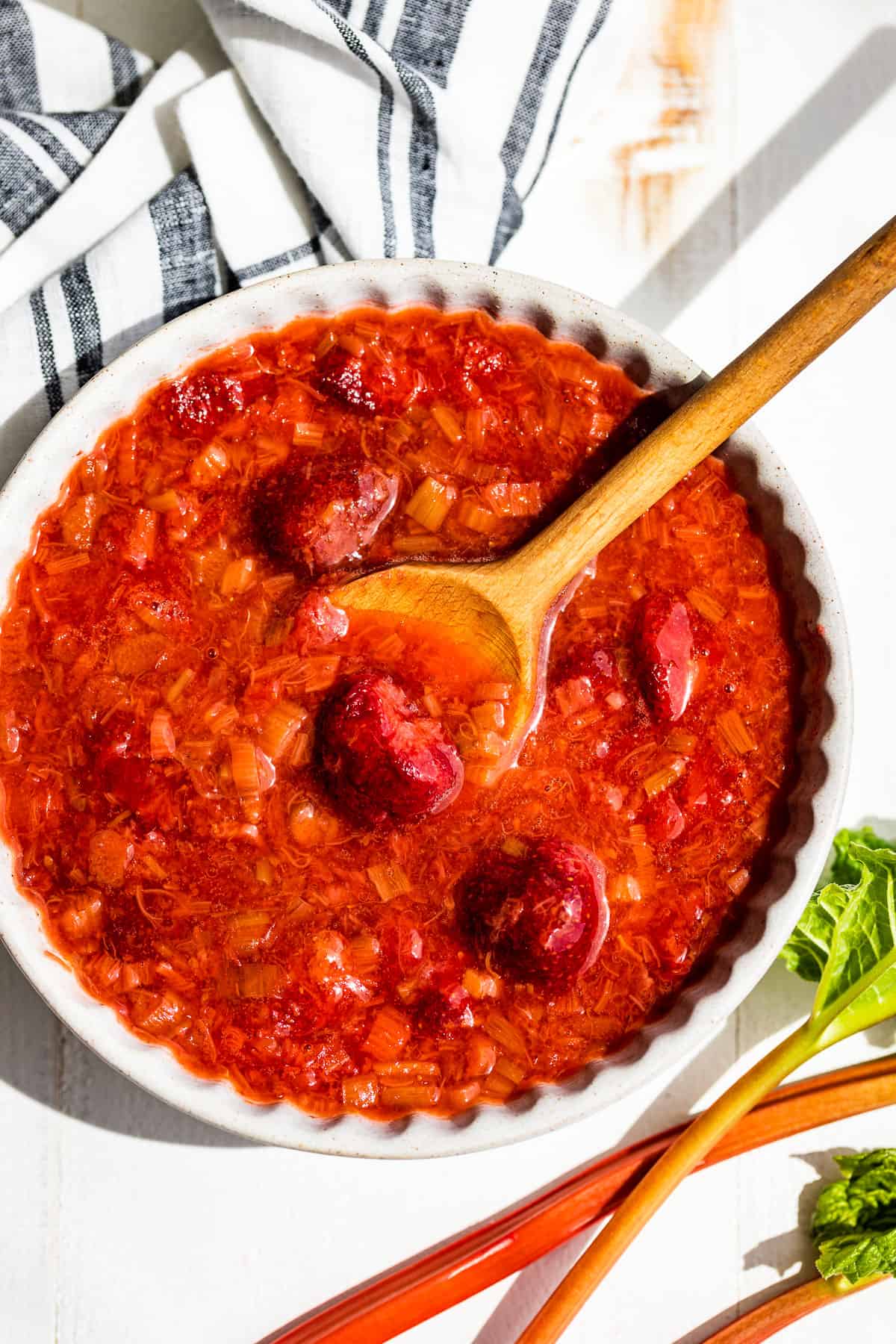 A straight down view of Strawberry Rhubarb Sauce in a grey pottery bowl with a wooden spoon.