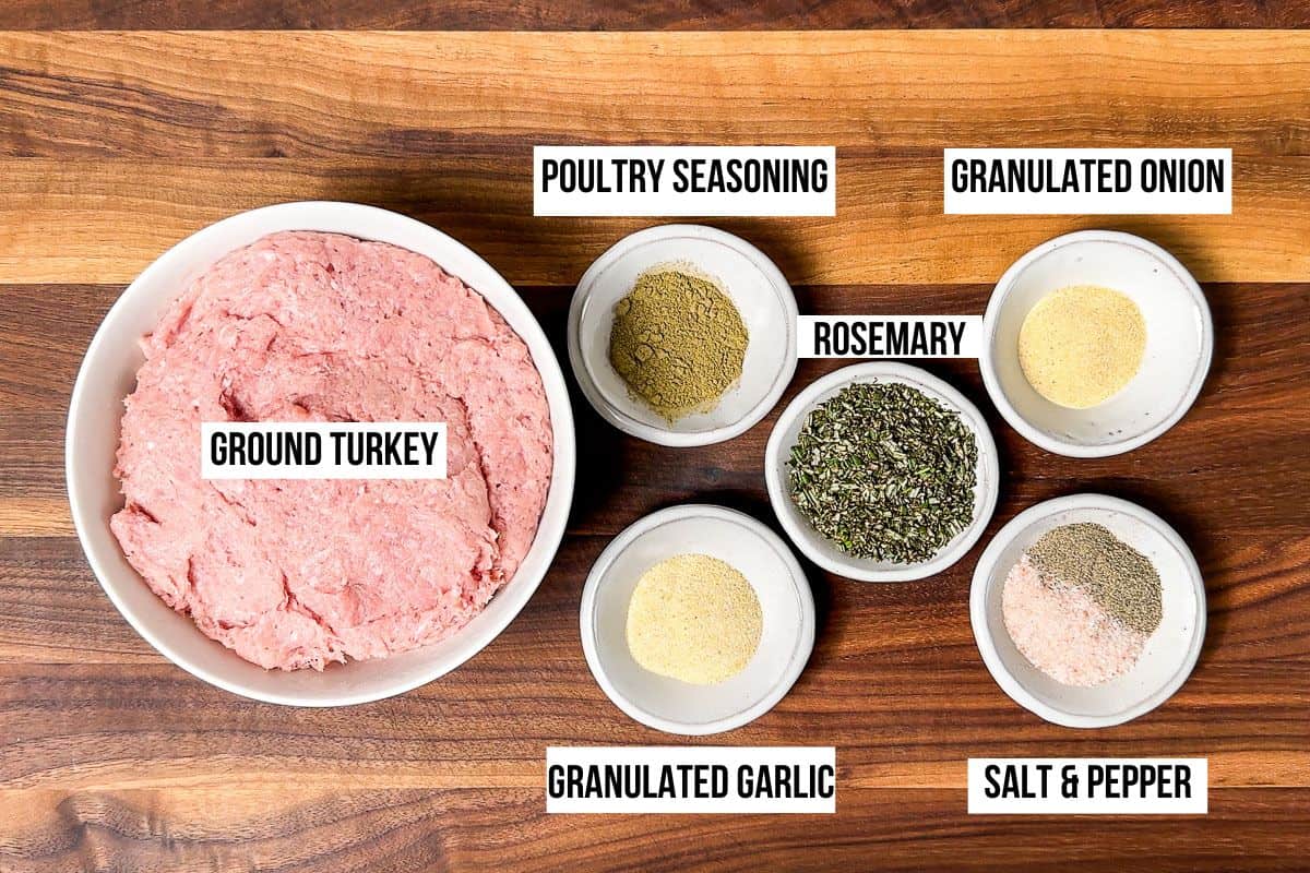 Ground turkey, fresh rosemary, garlic granules, onion granules, salt, pepper, and poultry seasoning in bowls on a wood cutting board.